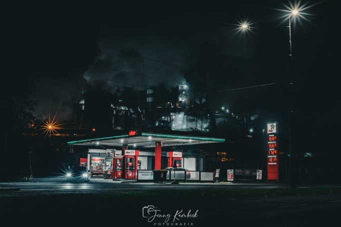 Moderne Tankstelle bei Nacht mit leuchtenden roten Akzenten und dunklem Hintergrund.