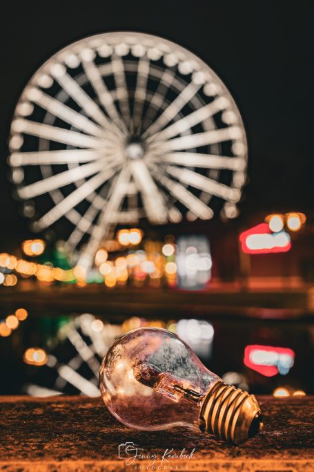 Glühbirne im Vordergrund, im Hintergrund ein Riesenrad bei Nacht.