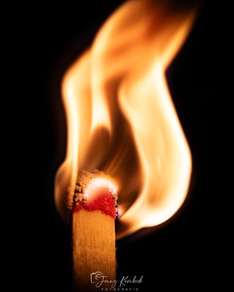 Brennende Zündholz mit heller Flamme auf schwarzem Hintergrund.