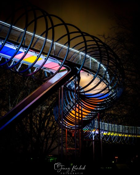 Bunte Lichteffekte entlang einer spiralförmigen Metallstruktur in der Nacht.