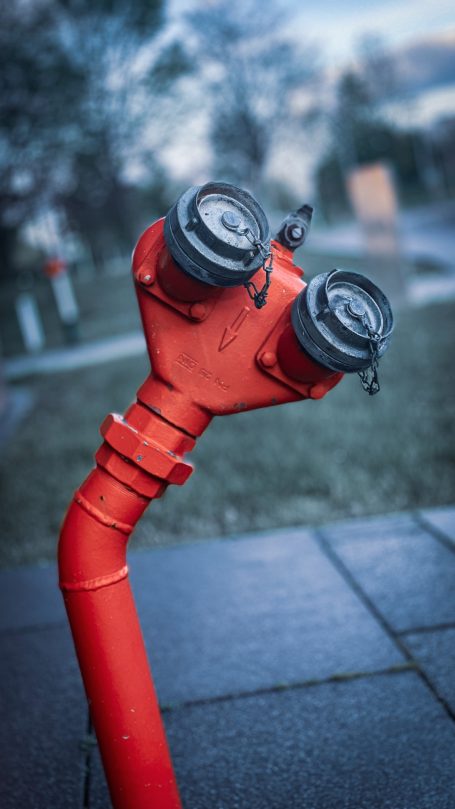 Roter Hydrant mit zwei Ausgängen, im Freien auf einem Gehweg.