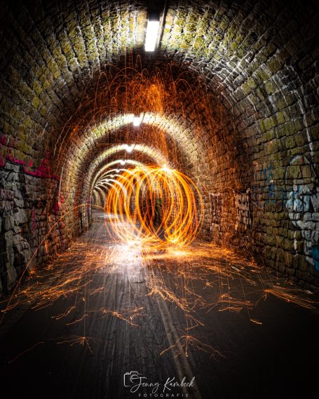 Ein dunkler Tunnel mit leuchtenden Lichtspuren und grauer Steinmauer.