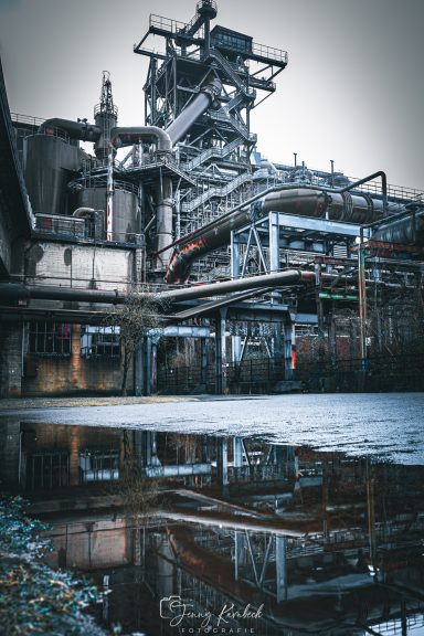 Industrielle Anlage mit Rohrleitungen und Reflexion im Wasser.