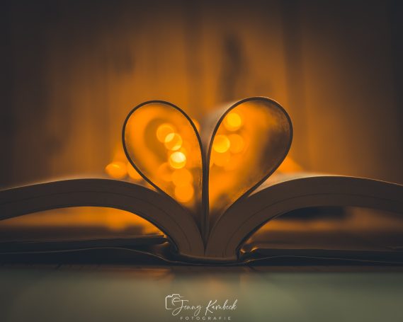 Ein aufgeschlagenes Buch formt ein Herz aus seinen Seiten, umgeben von warmem Licht.