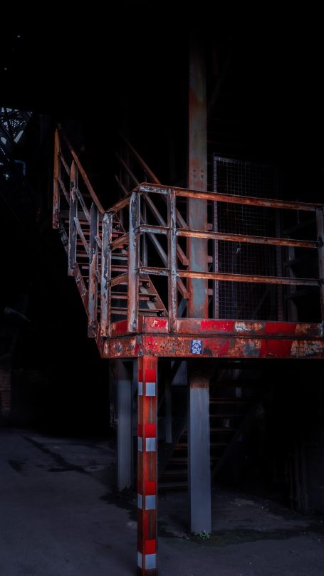 Rostige Treppe mit Geländer in dunkler Umgebung.