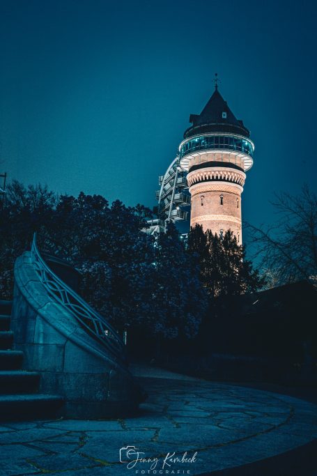 Nachtaufnahme eines beleuchteten Turms mit spiralförmigen Stufen im Vordergrund.