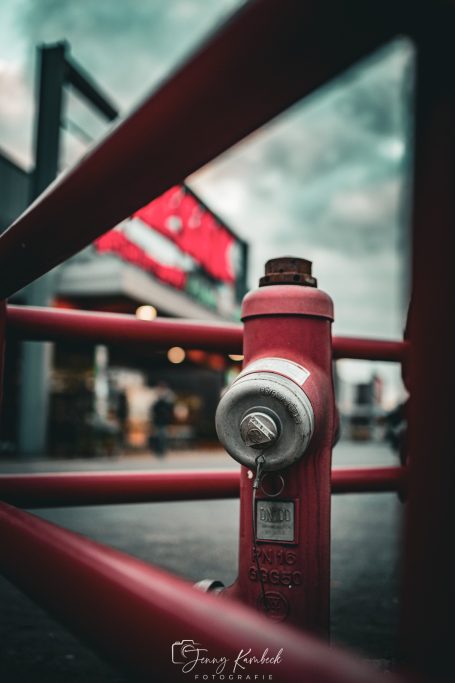 Rote Hydrant mit verschwommenem Hintergrund eines Gebäudes und grauem Himmel.