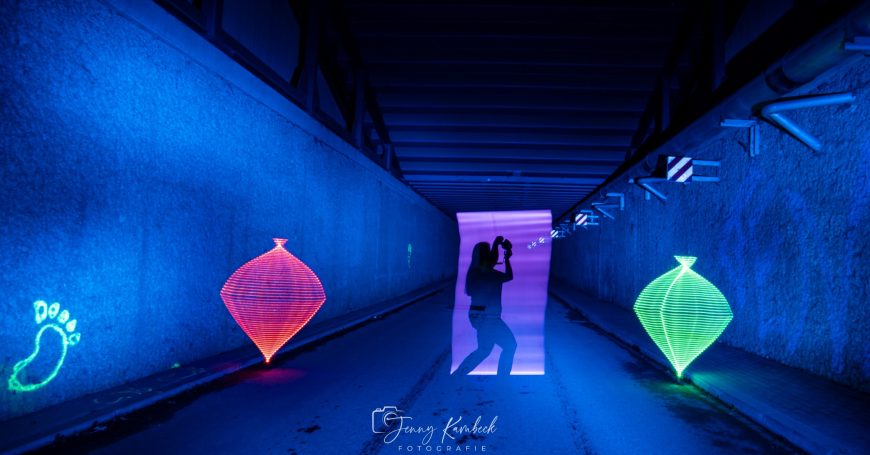 Siluette eines Paares in einem beleuchteten Tunnel mit bunten Lichtern.