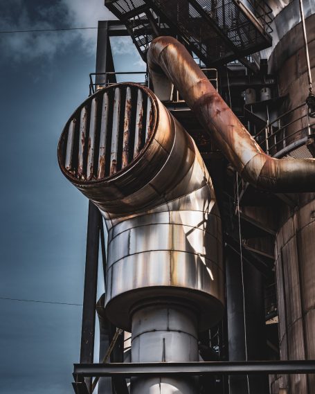 Rostige Rohre und Lüftungssystem eines Industriegebäudes vor einem bewölkten Himmel.