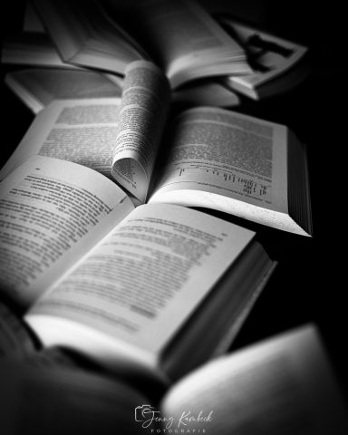 Mehrere aufgeschlagene Bücher liegen in verschiedenen Positionen auf einem Tisch.