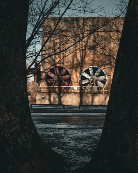 Große Ventilatoren an einer Wand, umgeben von schattigen Bäumen im Vordergrund.